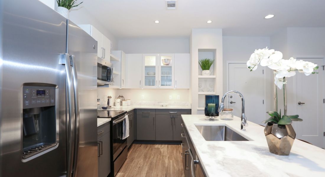 The District Flats apartment kitchen featuring large marble kitchen island, stainless steel appliances and white cabinets