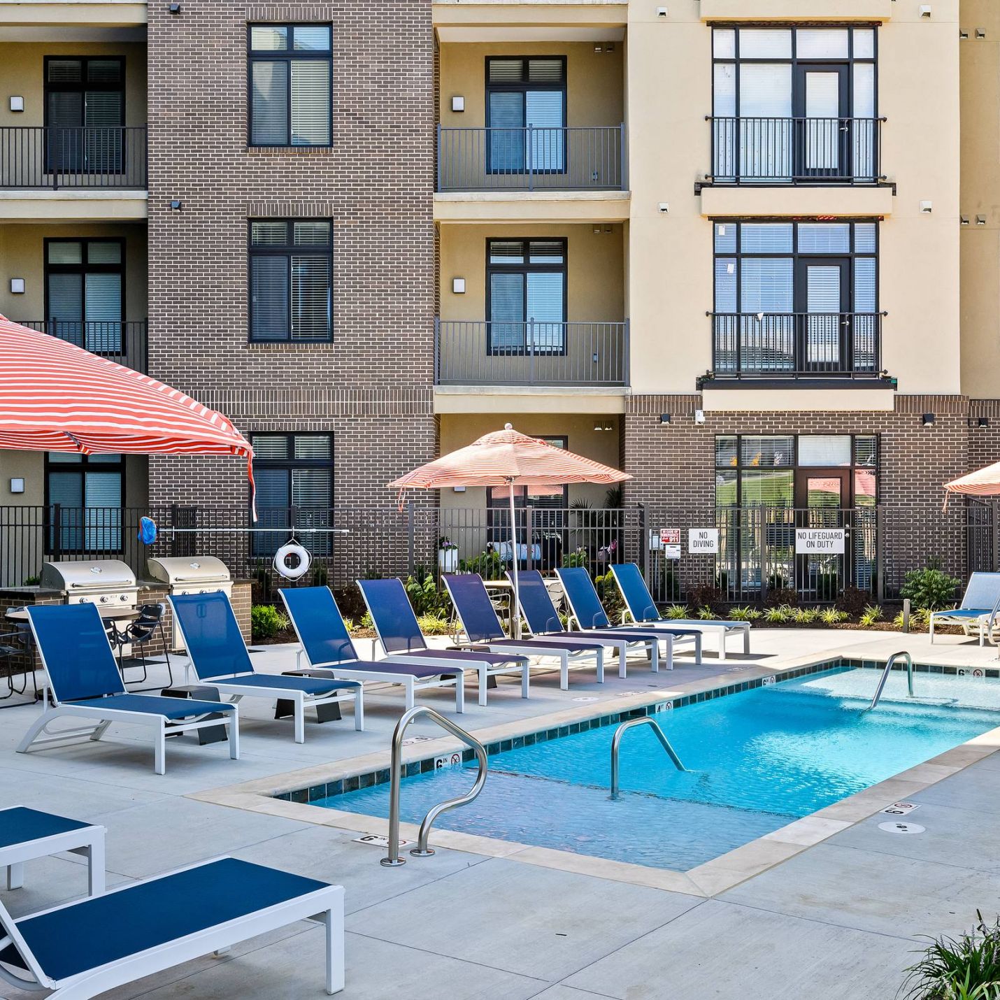 The District Flats apartment community pool with lounge chairs and nearby grills